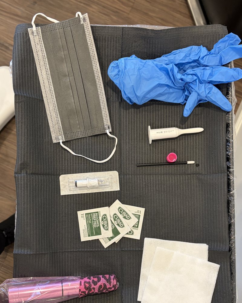 A setup tray in Ella's studio before a session: a face mask, blue gloves, alcohol pads, folded gauze and the machine still in its wrap, laid out on a black towel.