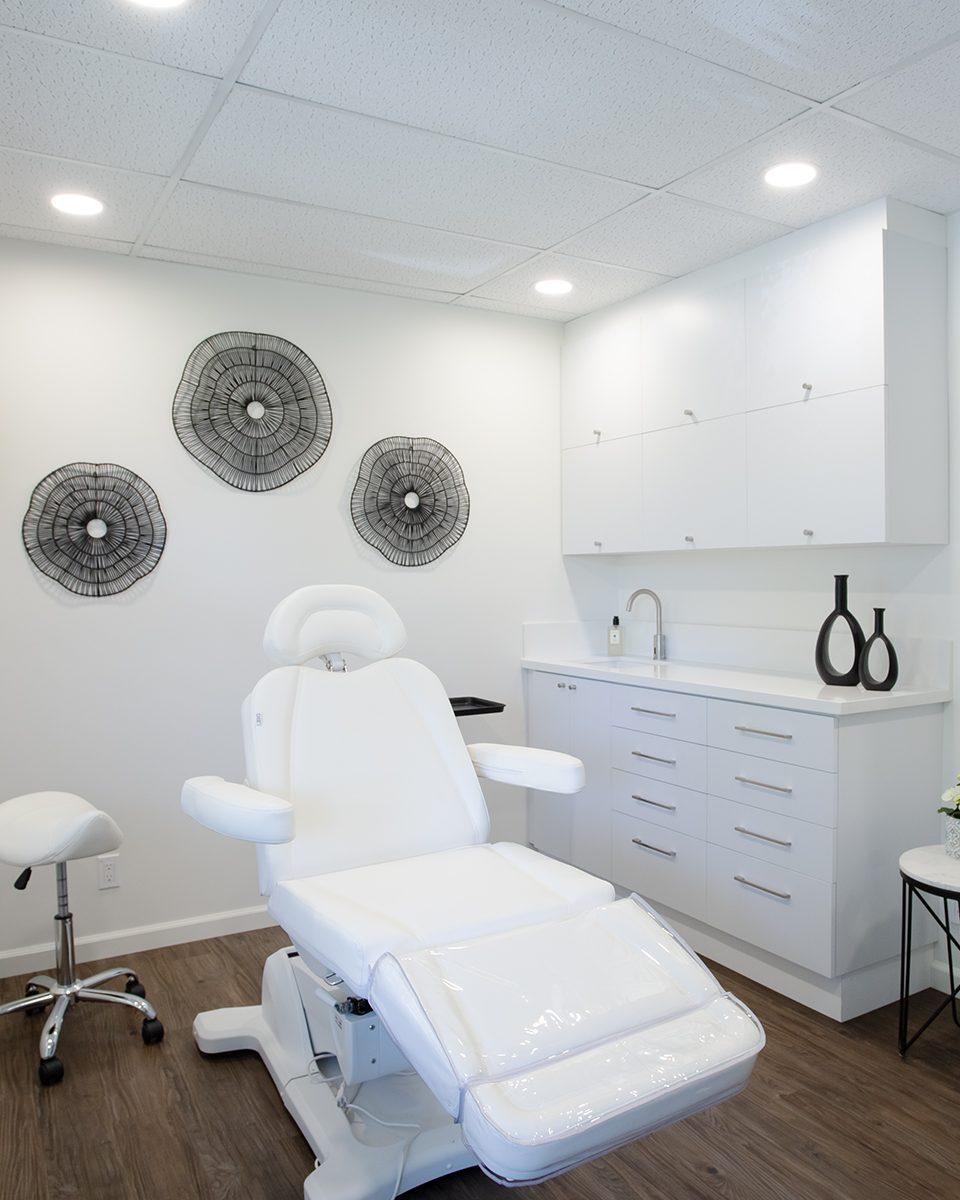 The bright white studio room: a white reclining chair and stool, white cabinets, three black wire wall discs, a hanging plant by the window and a tall mirror.